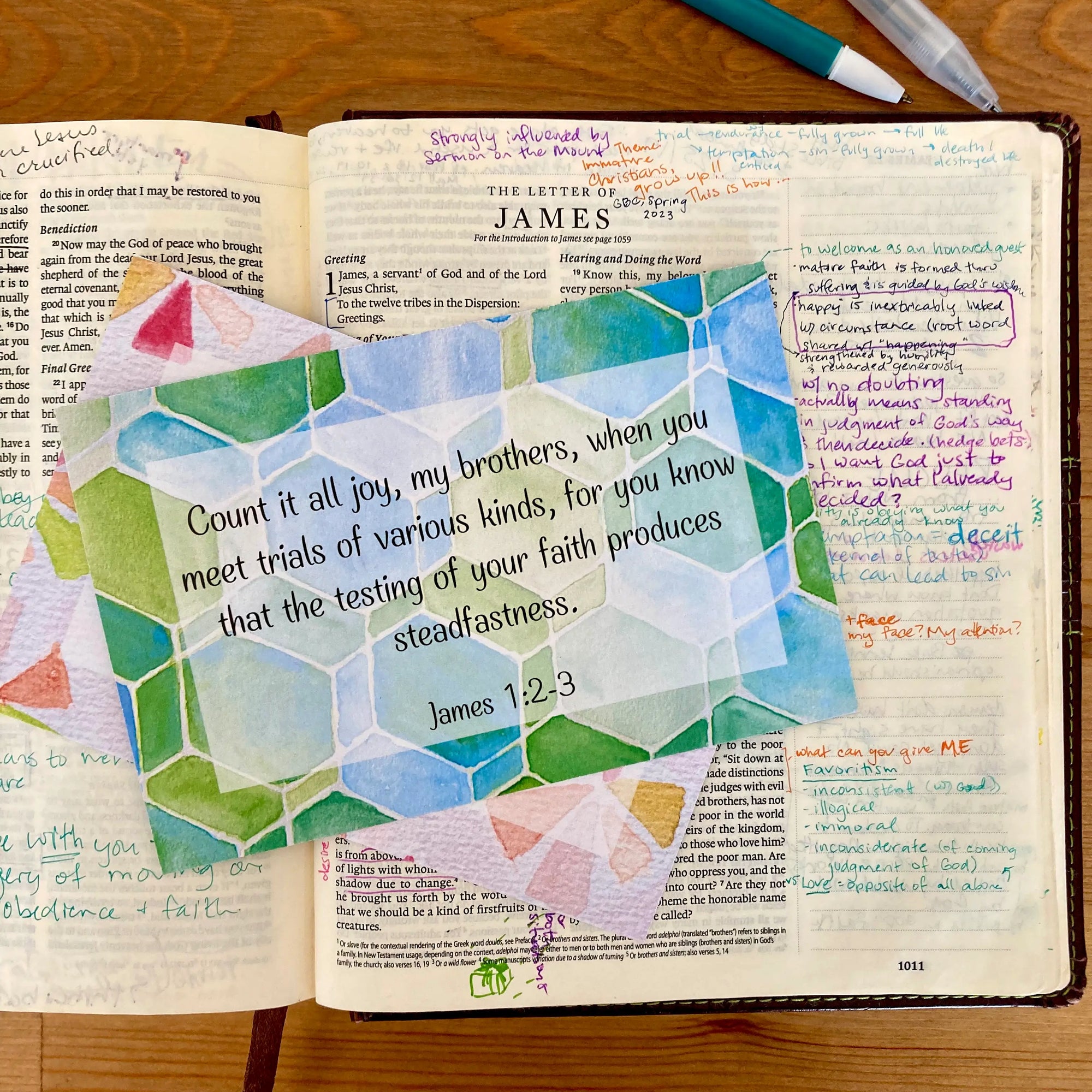 Open Bible with colorful geometric design and text on a wooden surface. Card lists James 1:2-3 -- consider it pure joy...