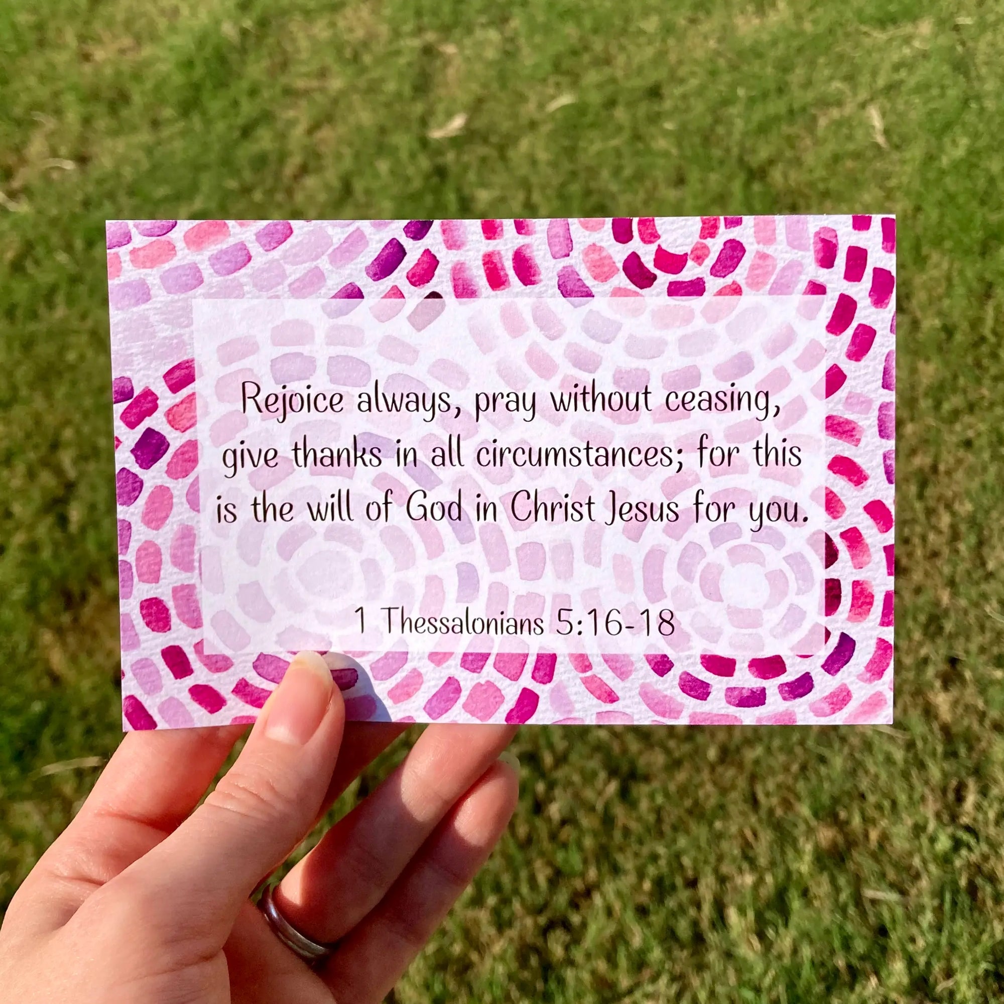 Hand holding a vibrant geometric card with a Bible verse about joy against a grassy background