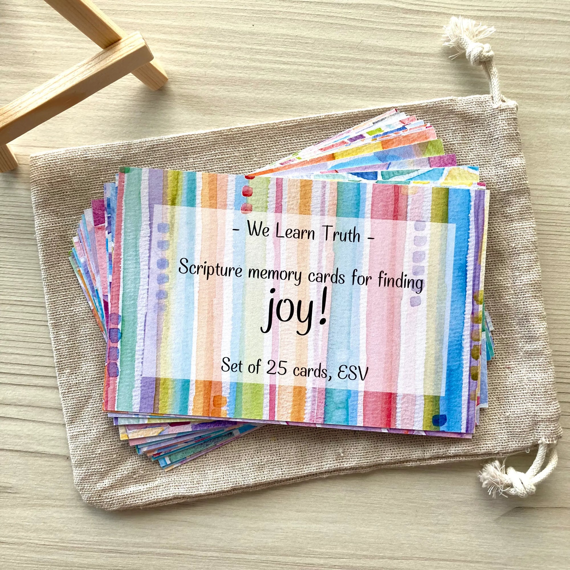 Set of colorful Scripture memory cards with text on a beige drawstring bag next to a display easel on the side.