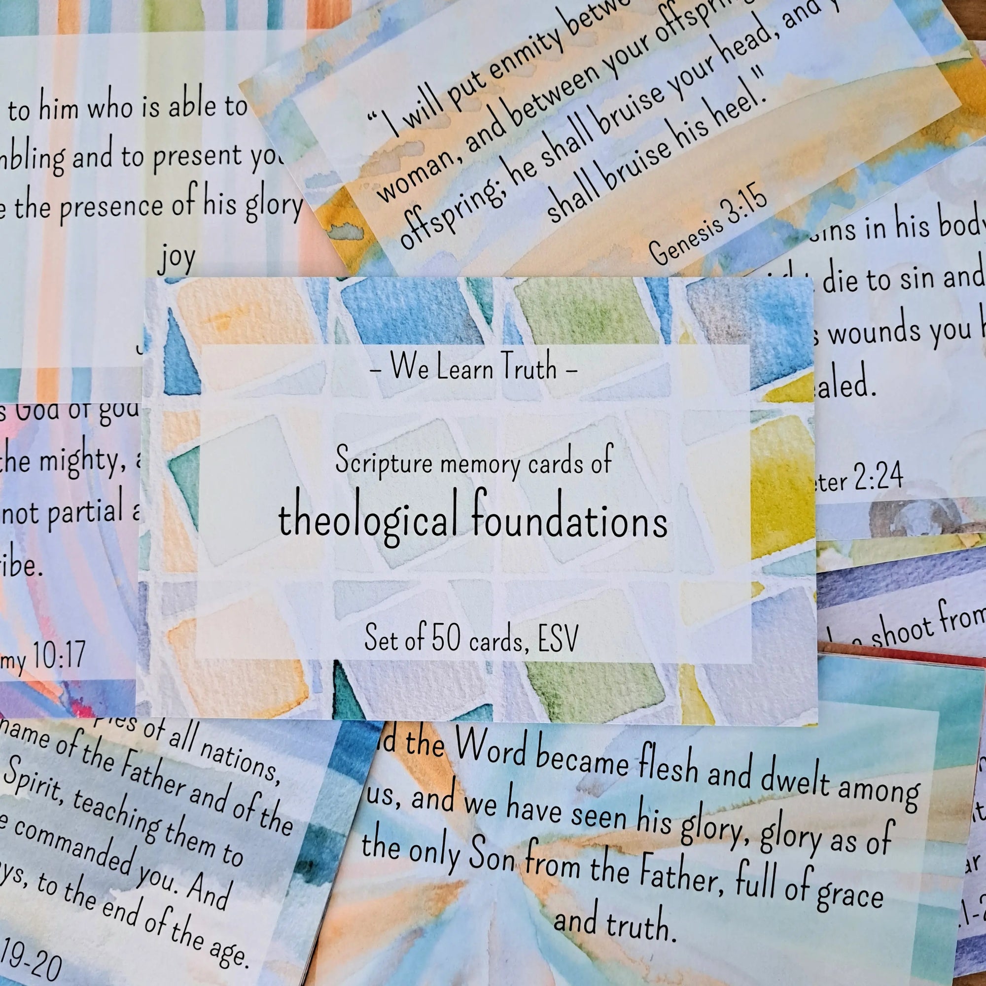 A set of 50 scripture memory cards with watercolor designs, featuring the text "We Learn Truth - Scripture memory cards of theological foundations, Set of 50 cards, ESV" prominently displayed, surrounded by other cards with various Bible verses, arranged on a flat surface