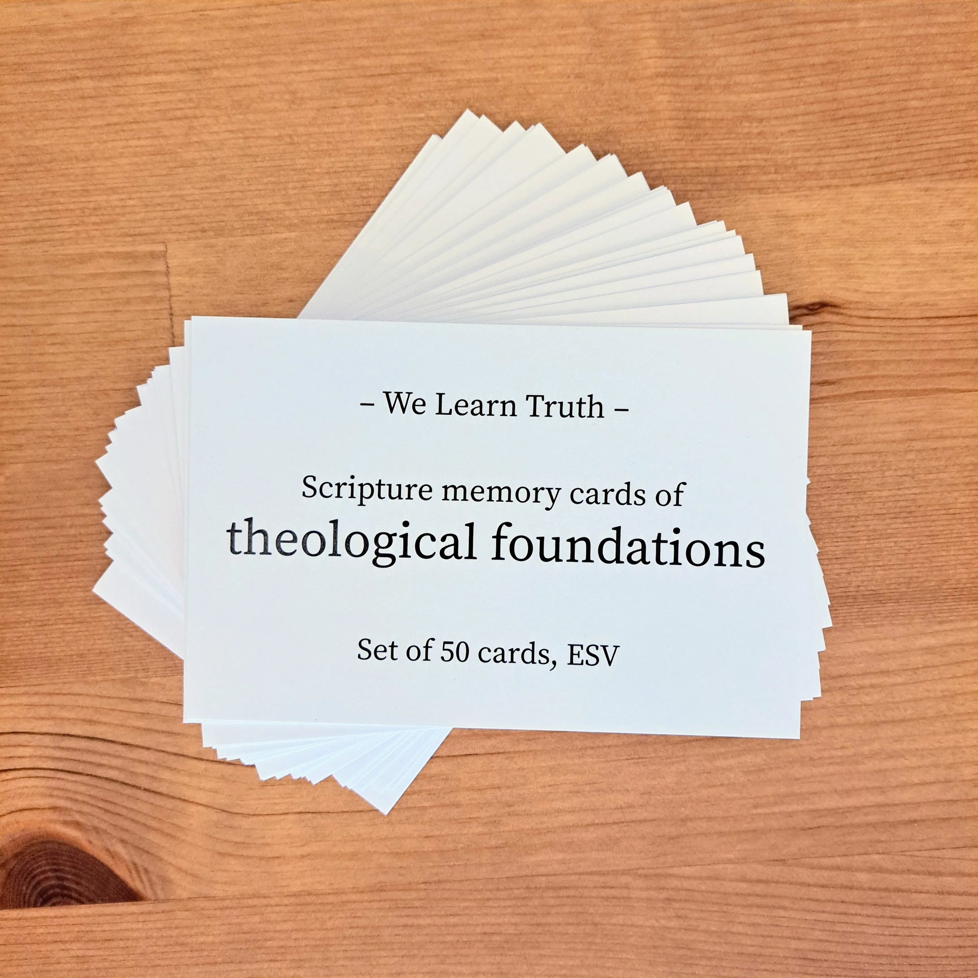 A fanned stack of white scripture memory cards labeled "We Learn Truth - Scripture memory cards of theological foundations, Set of 50 cards, ESV" displayed on a wooden surface