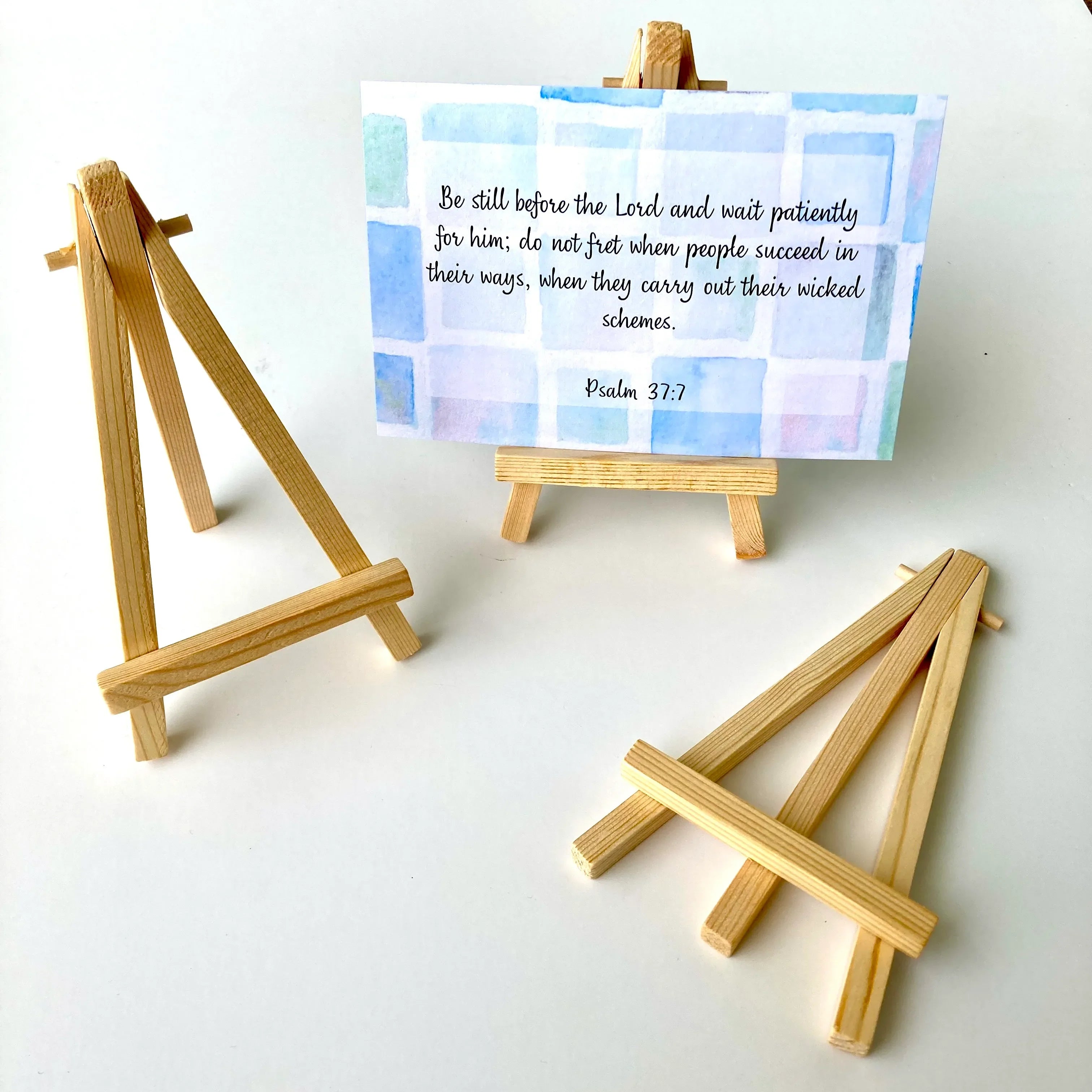 A simple wooden stand with a minimalist design, made of light wood pieces, placed on a wooden surface.