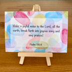 Colorful card with Psalm 98:4 text on a wooden easel.
