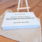 A stack of white scripture memory cards labeled "We Learn Truth - Scripture memory cards of theological foundations, Set of 50 cards, ESV" displayed on a wooden stand, with a canvas pouch on a wooden surface