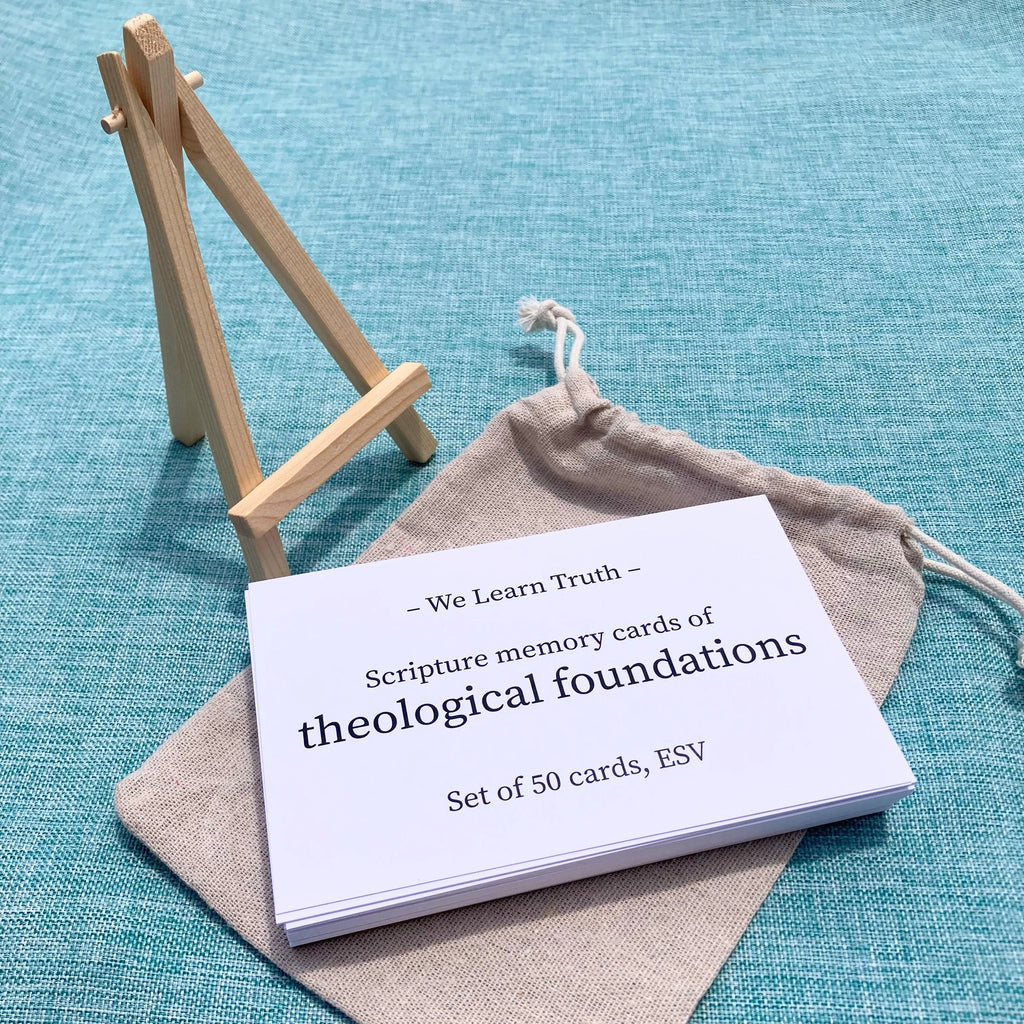 A stack of white scripture memory cards labeled "We Learn Truth - Scripture memory cards of theological foundations, Set of 50 cards, ESV" on a teal fabric, with a canvas pouch and wooden stand nearby